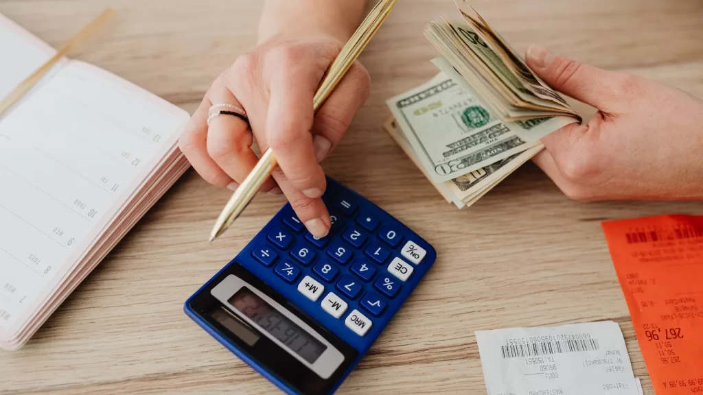 Image of a person counting cash with a notepad and a calculator on the table to denote capital loan services for commercial vehicle trip expenses.